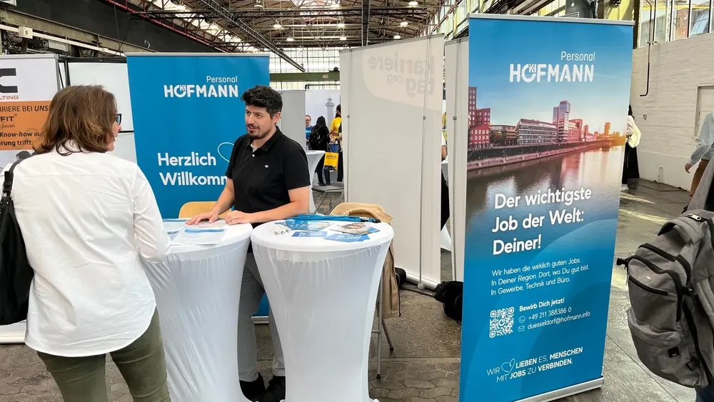Hofmann Personal Messestand mit Beratungsgespräch an Stehtischen vor blauem Branding