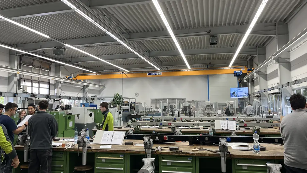 Viele Mitarbeitende arbeiten konzentriert an Maschinen und Werkbänken in heller Umgebung