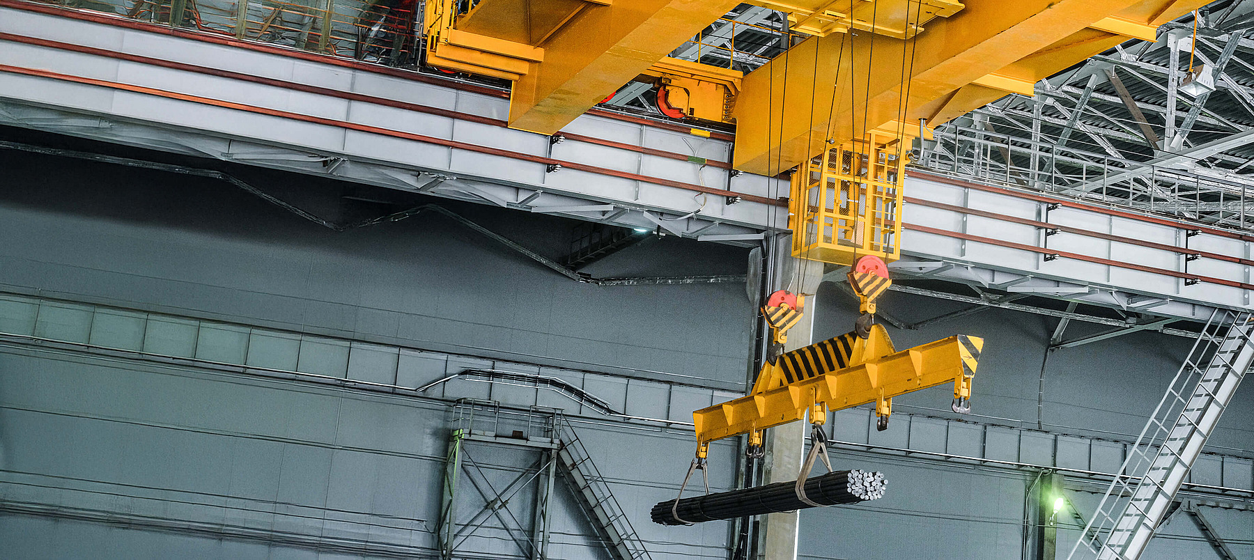 Gelber Industriekran mit Greifarm hebt Metallträger in moderner Produktionshalle.