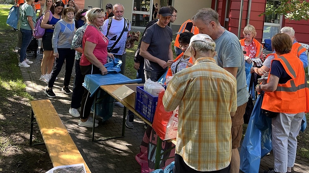 Gruppe von Ehrenamtlichen bei einer Müllsammelaktion, ausgestattet mit Warnwesten und Müllsäcken im Außenbereich