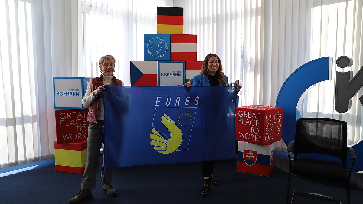 Sonja Heinrich, Mitglied des Executive Committee von Hofmann Personal, hält gemeinsam mit einer weiteren Frau eine EURES-Flagge beim EURES-Jahrestreffen 2026.