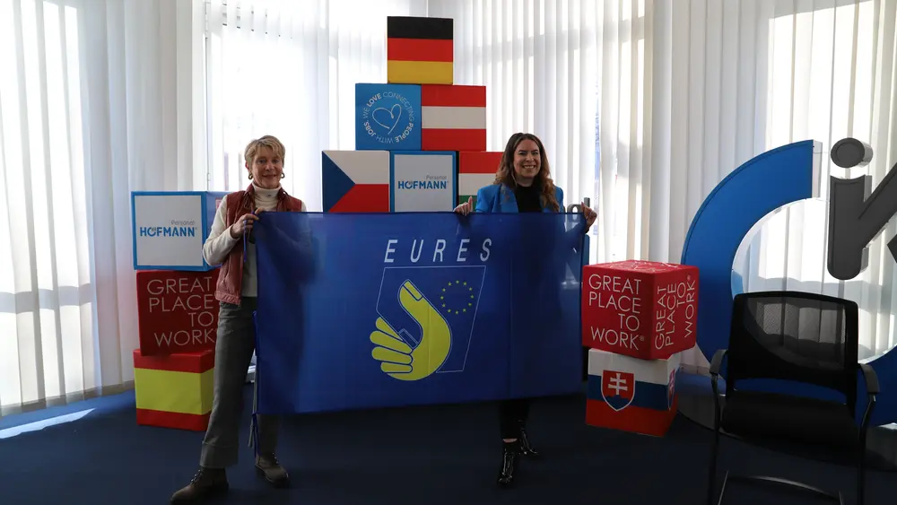 Sonja Heinrich, Mitglied des Executive Committee von Hofmann Personal, hält gemeinsam mit einer weiteren Frau eine EURES-Flagge beim EURES-Jahrestreffen 2026.