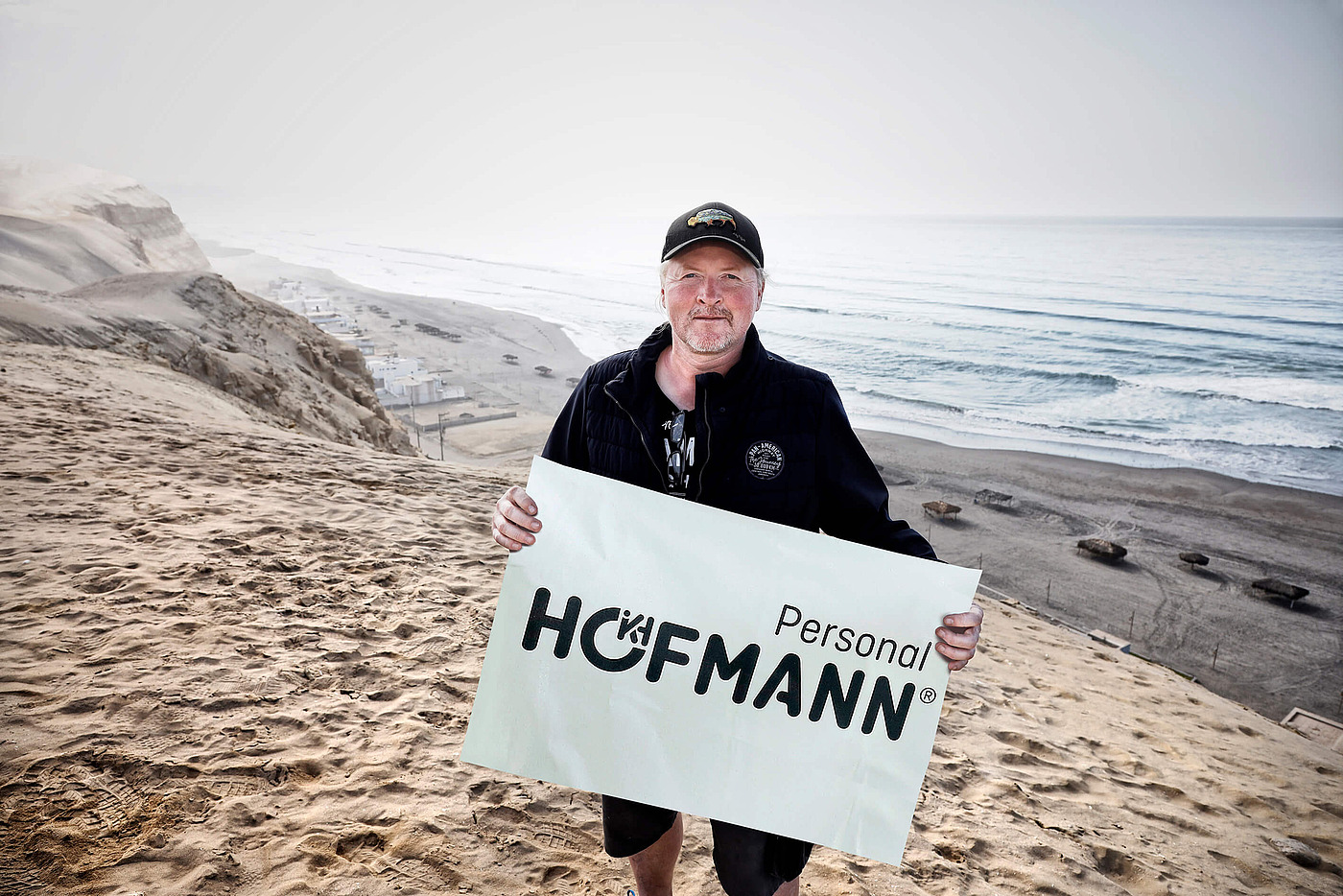 Markenbotschafter Joey Kelly mit Hofmann-Schild an einem sandigen Strand in Peru.