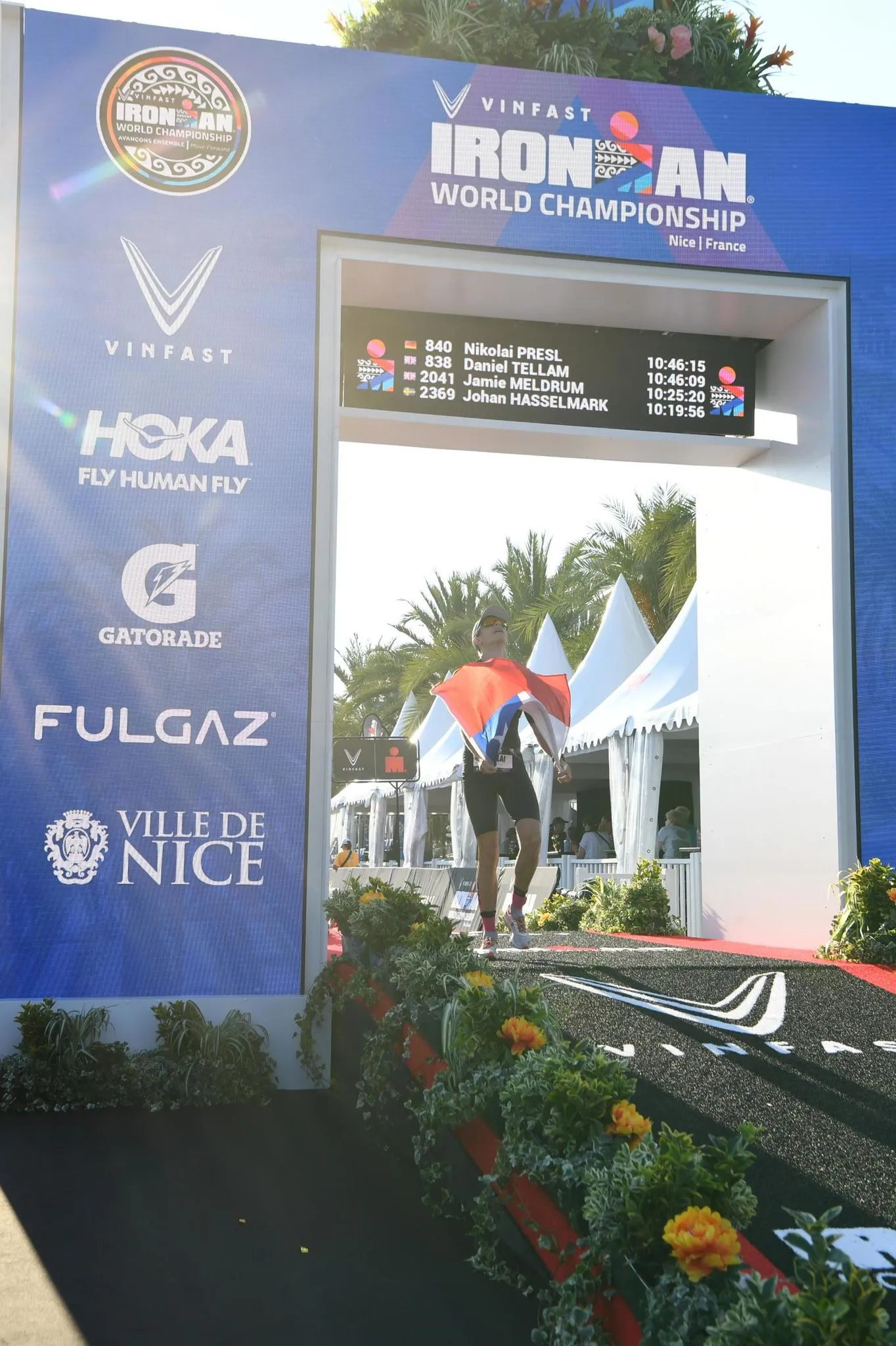 Professioneller Triathlet erreicht die Ziellinie bei einem Wettkampf, Symbol für Ehrgeiz und Entschlossenheit bei Hofmann Personal.  