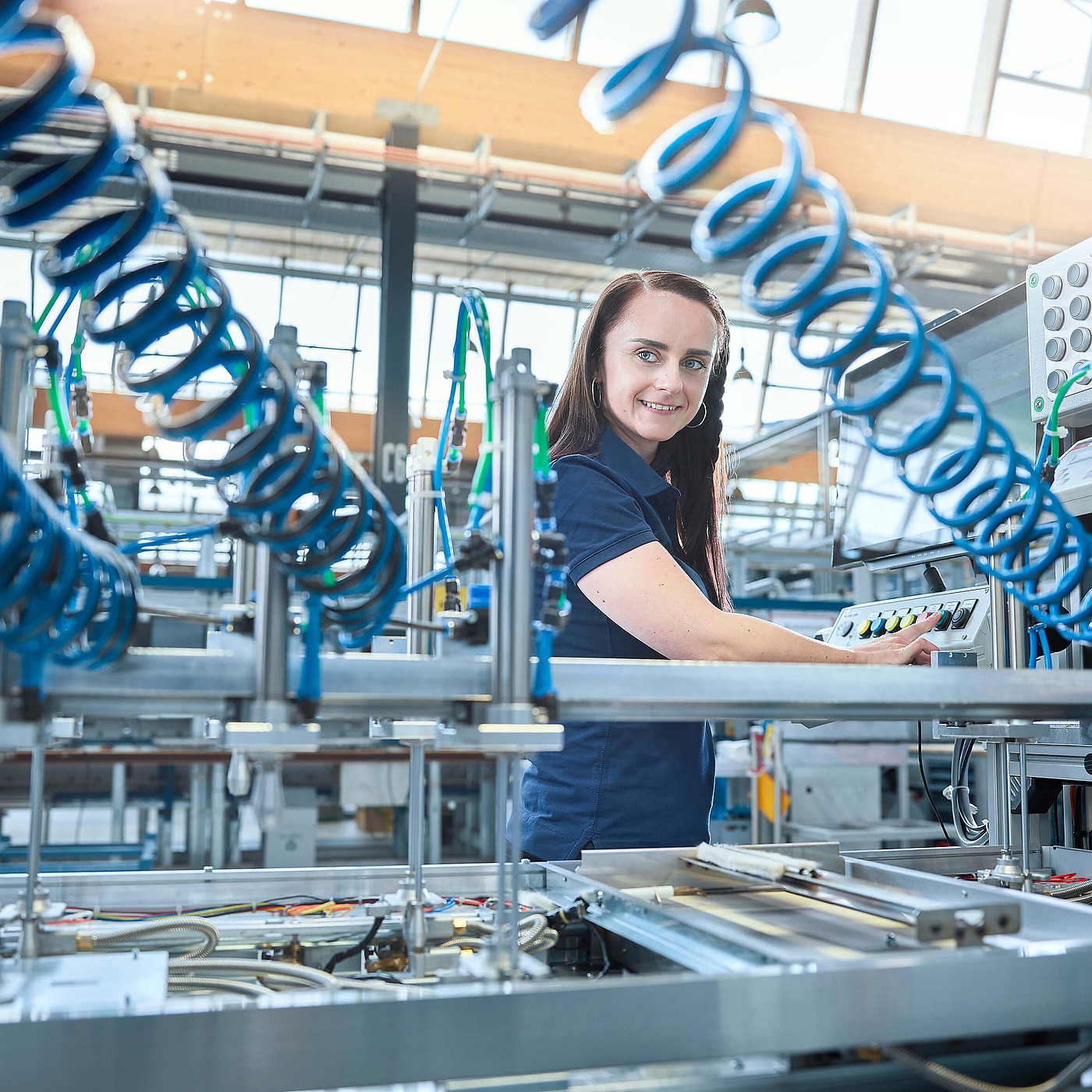 Mitarbeiterin steuert fokussiert eine automatisierte Produktionsanlage mit Schläuchen in einer Produktionshalle.