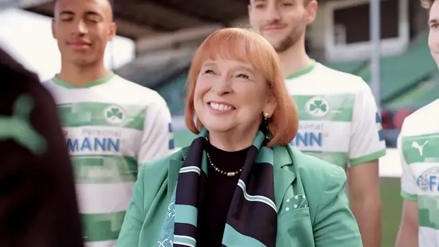 Ingrid Hofmann, Geschäftsführerin, im grünen Outfit mit Spielern der SpVgg Greuther Fürth im Stadion.