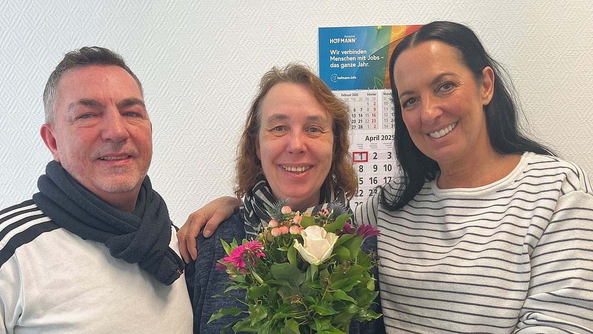 Einer Frau im blauen Pullover werden Blumen überreicht, symbolisch für Teamgeist und wertschätzende Kommunikation bei Hofmann Personal.