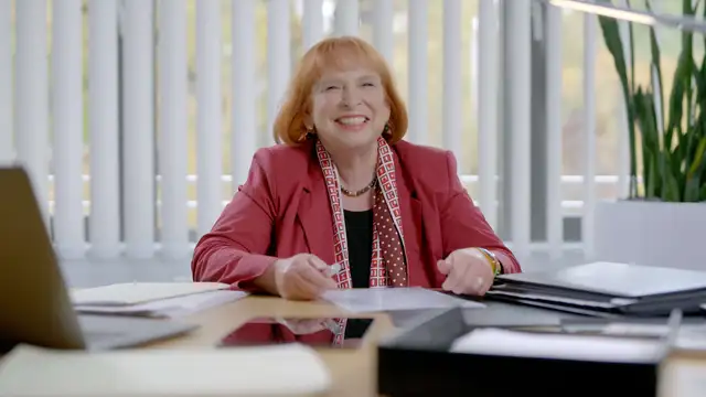 Ingrid Hofmann, Geschäftsführerin, im roten Blazer sitzt im Büro am Schreibtisch und liest Unterlagen.