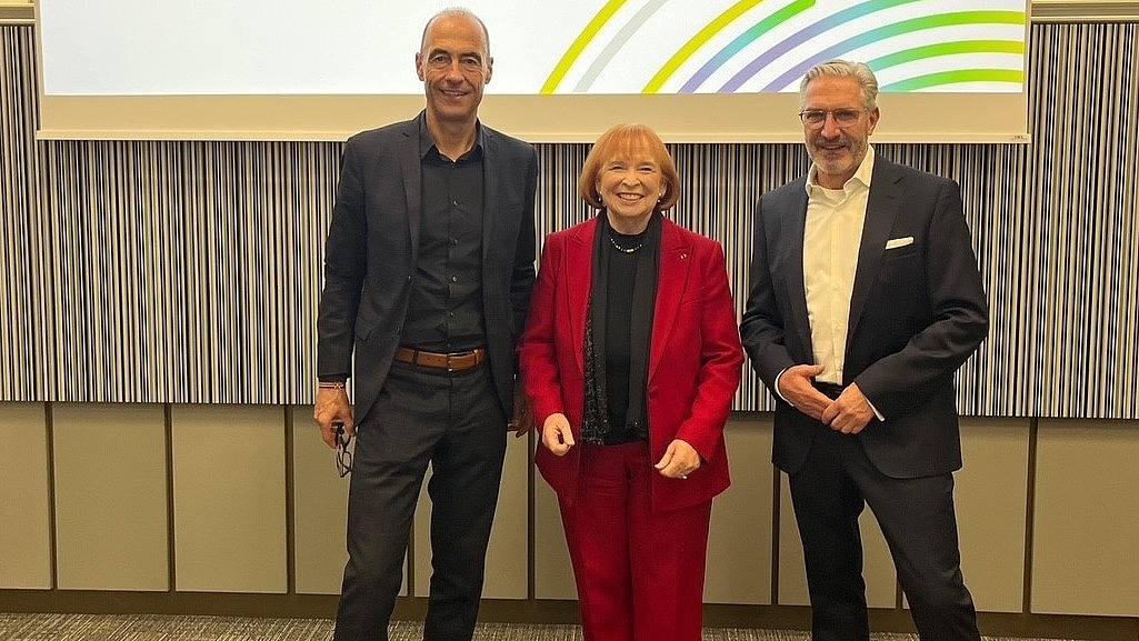 Ingrid Hofmann, Gründerin von Hofmann Personal, steht beim 10 Interdisziplinären Forum zur Zeitarbeit neben zwei Mitarbeitern in Anzügen.