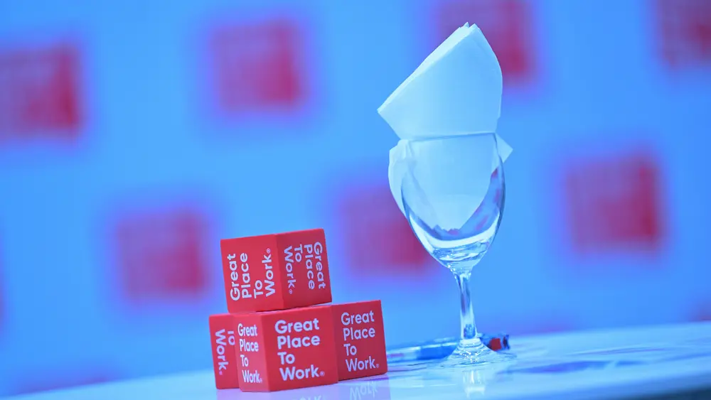 Kleine rote Great-Place-To-Work-Würfel neben einem edlem Glass. 