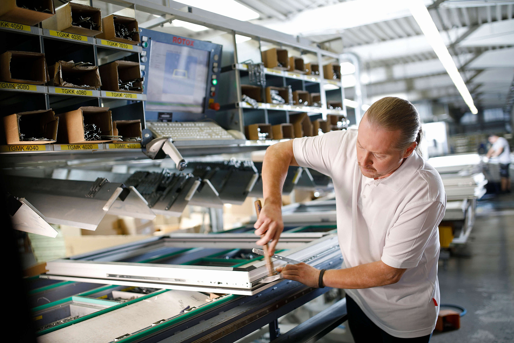Joey Kelly in weißem Hemd beugt sich über eine Maschine in einer Industriehalle