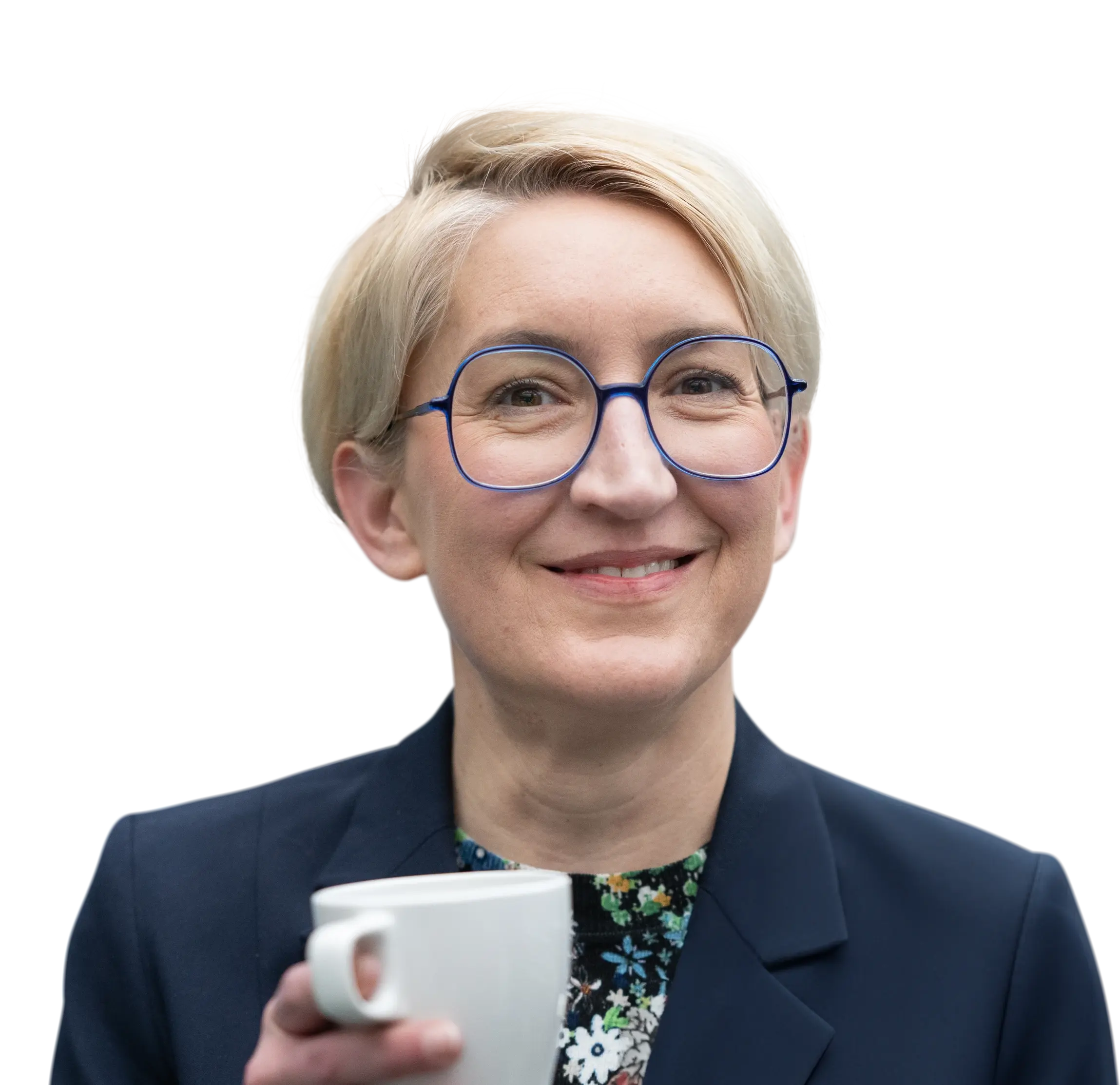 Lächelnde Mitarbeiterin mit blauer Brille und weißer Tasse in der Hand.