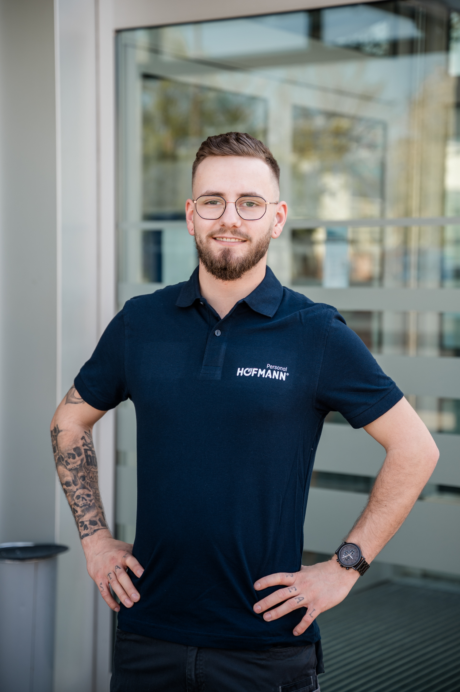 Hofmann-Personal-Mitarbeiter im Firmenpoloshirt steht vor dem Standort und schaut freundlich in die Kamera