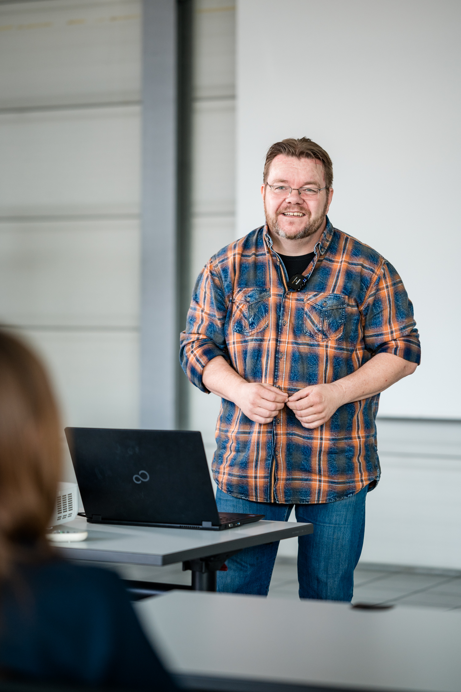 Dozent steht vor Laptop und spricht zu Teilnehmern in einem Schulungsraum